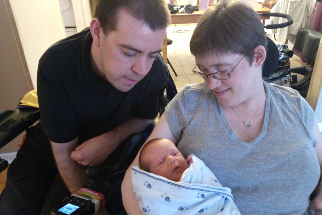 A couple with a disability in wheelchairs holding their infant child.