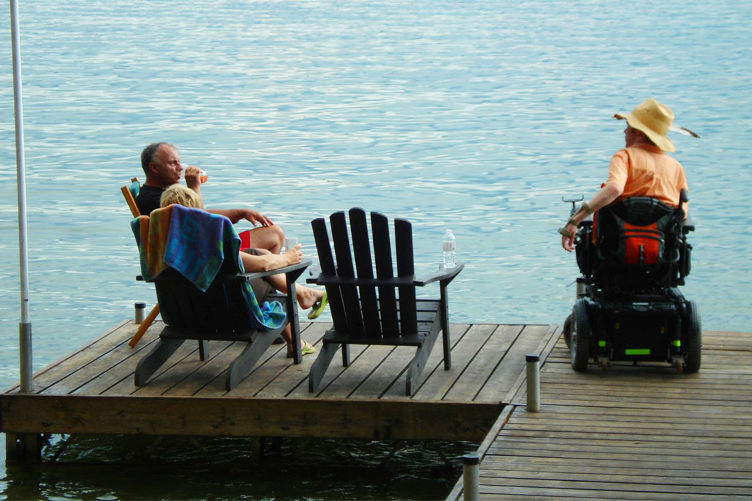 Man sitting in powered wheelchair hanging out with two others in chairs on a dock.