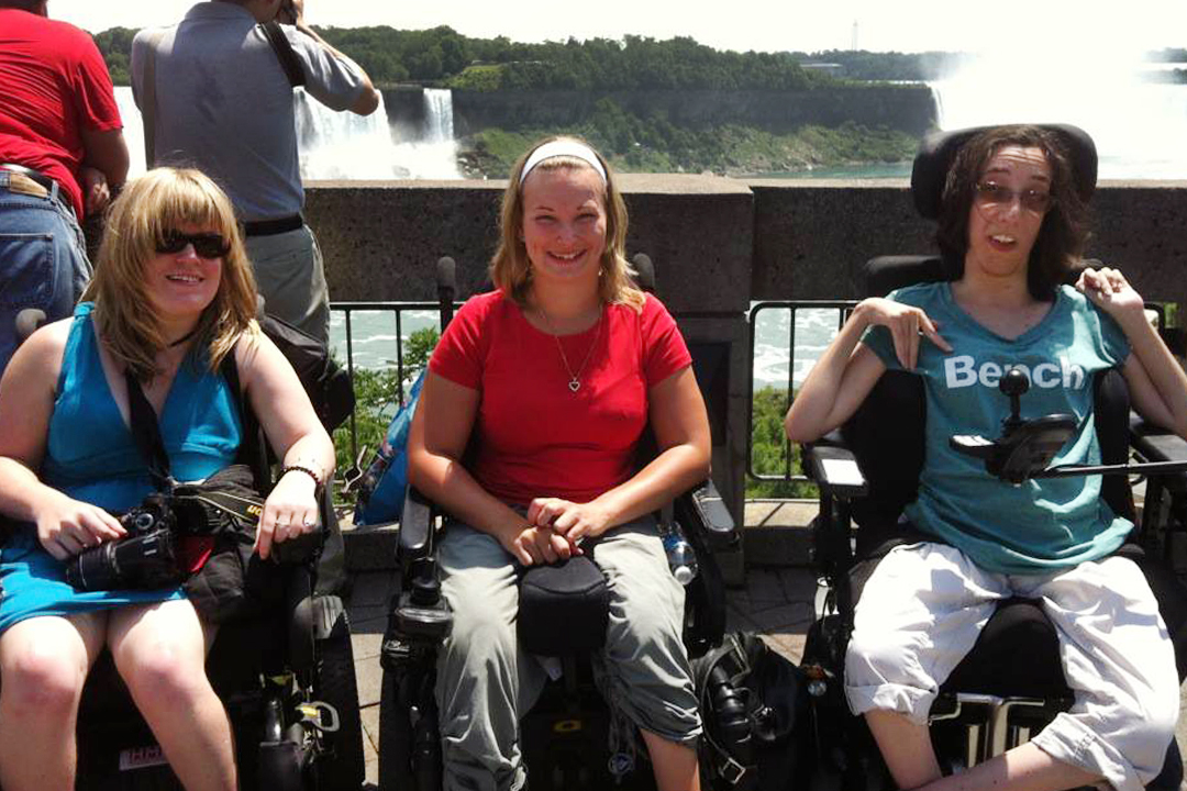 Man behind woman in wheelchair with steel drum band in background.