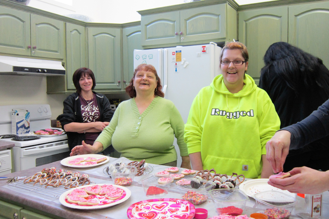 Three women in front of table of pink heart shaped cookies.