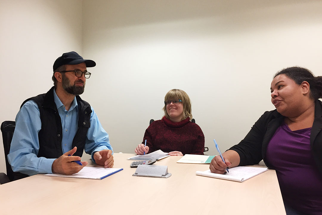 Three people sitting around a meeting table talking.