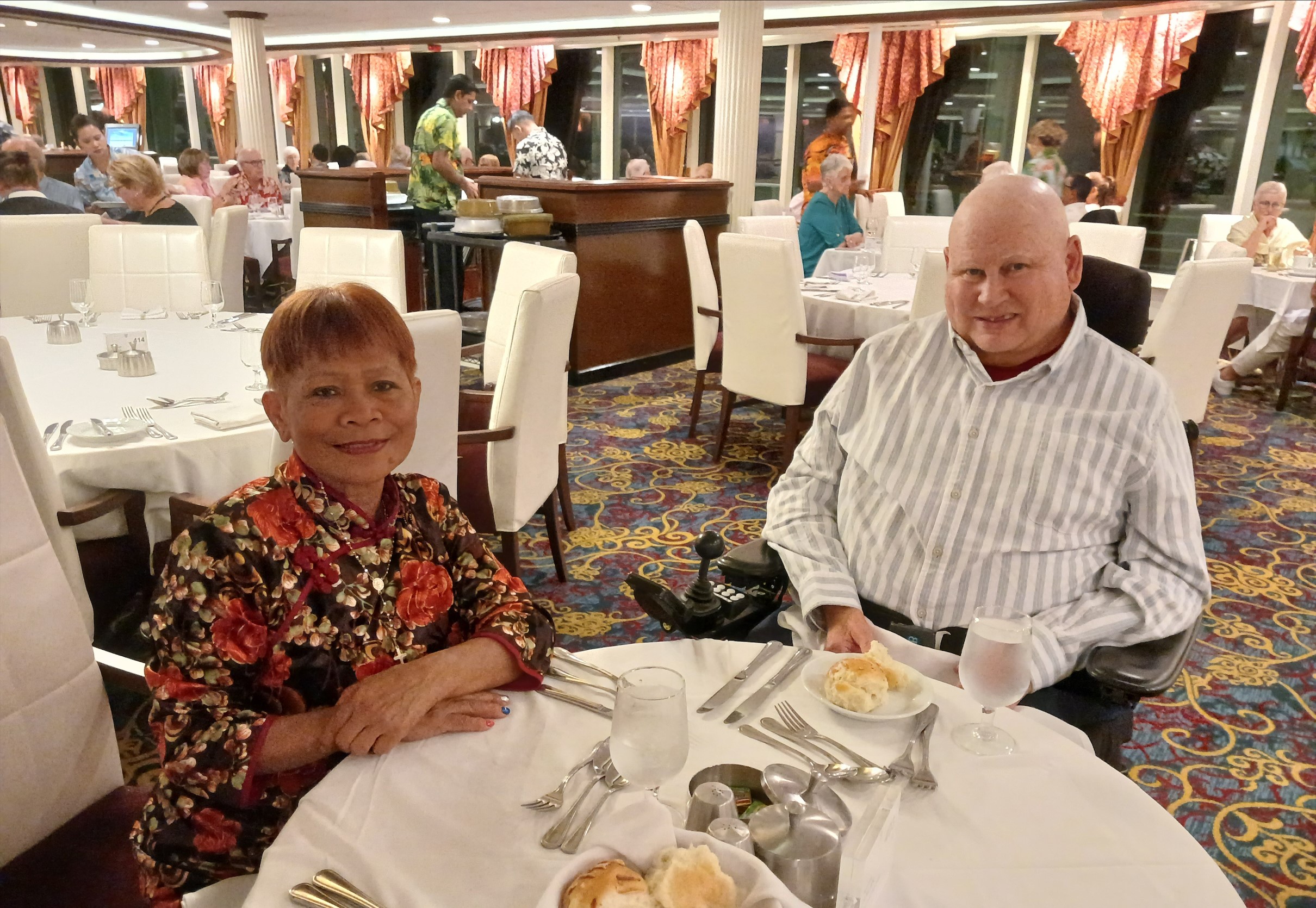 Donald and Edna sit at a table covered with a white tablecloth for a meal. They are in an elegant dining room.