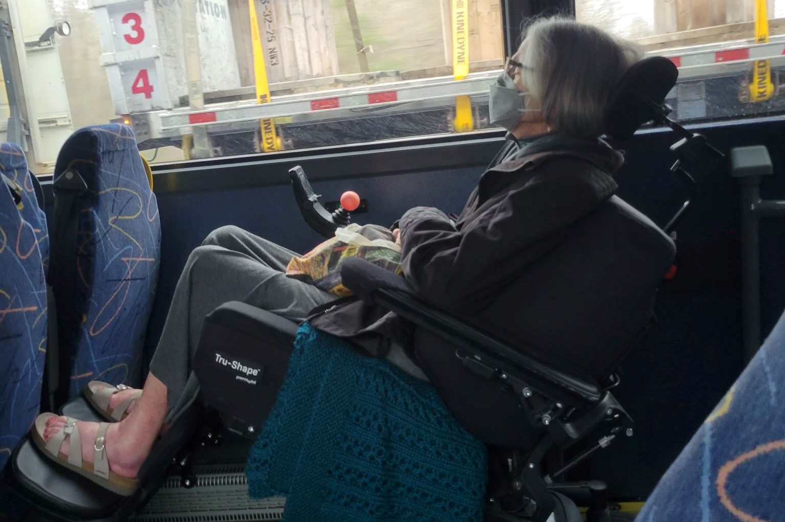 Dorothy is seated in her powerchair inside the Megabus and looking out the window.