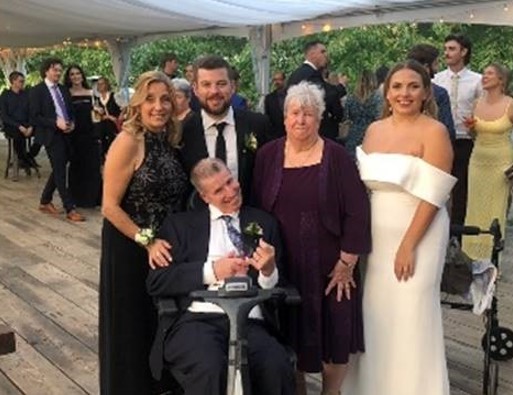 John and his family, including his daughter, pose for the camera outside, under a covered area.