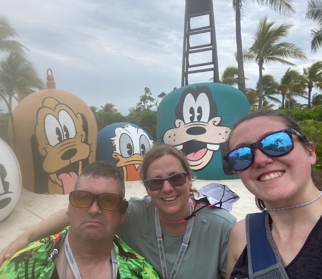 Mike Tkachuk and two others, all wearing sunglasses, are posing outside in front of large images of several Disney characters.