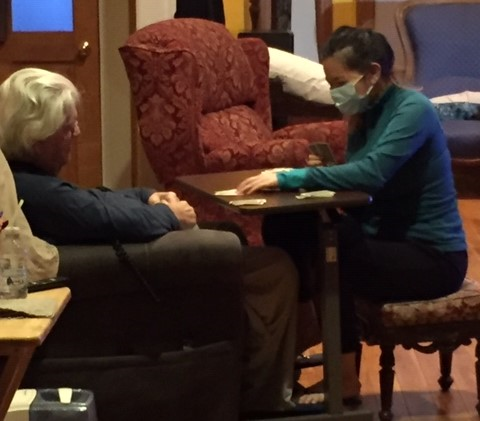 Oliver and attendant Thao Vo play cards, seated across from each other at a small table in a living room.