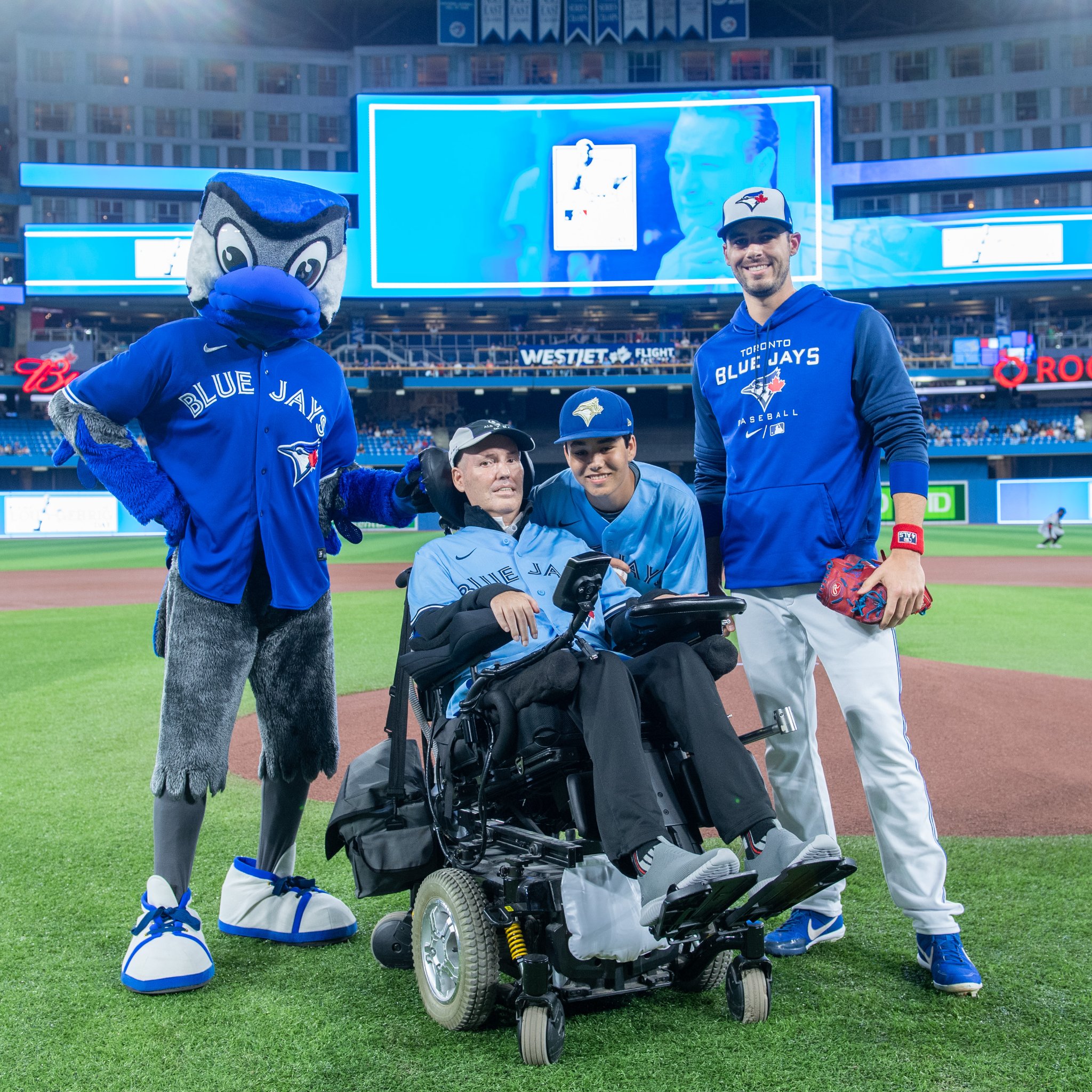 Peter and his son, Zachary, posing on the baseball pitch with Blue Jays pitcher, Julian Merryweather, and mascot, Ace.